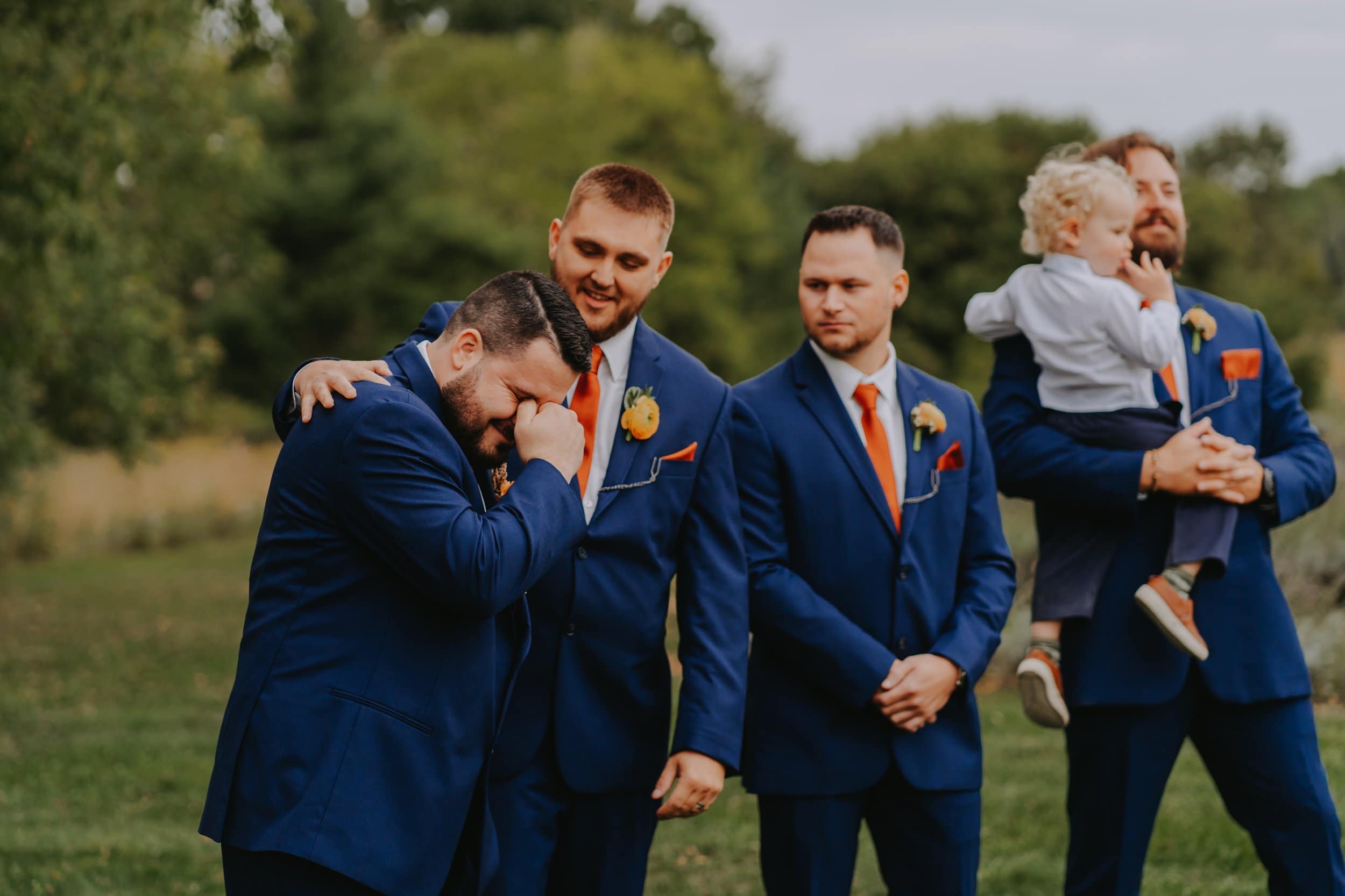 Wedding photography. The groom is holding back tears and his best man is comforting him