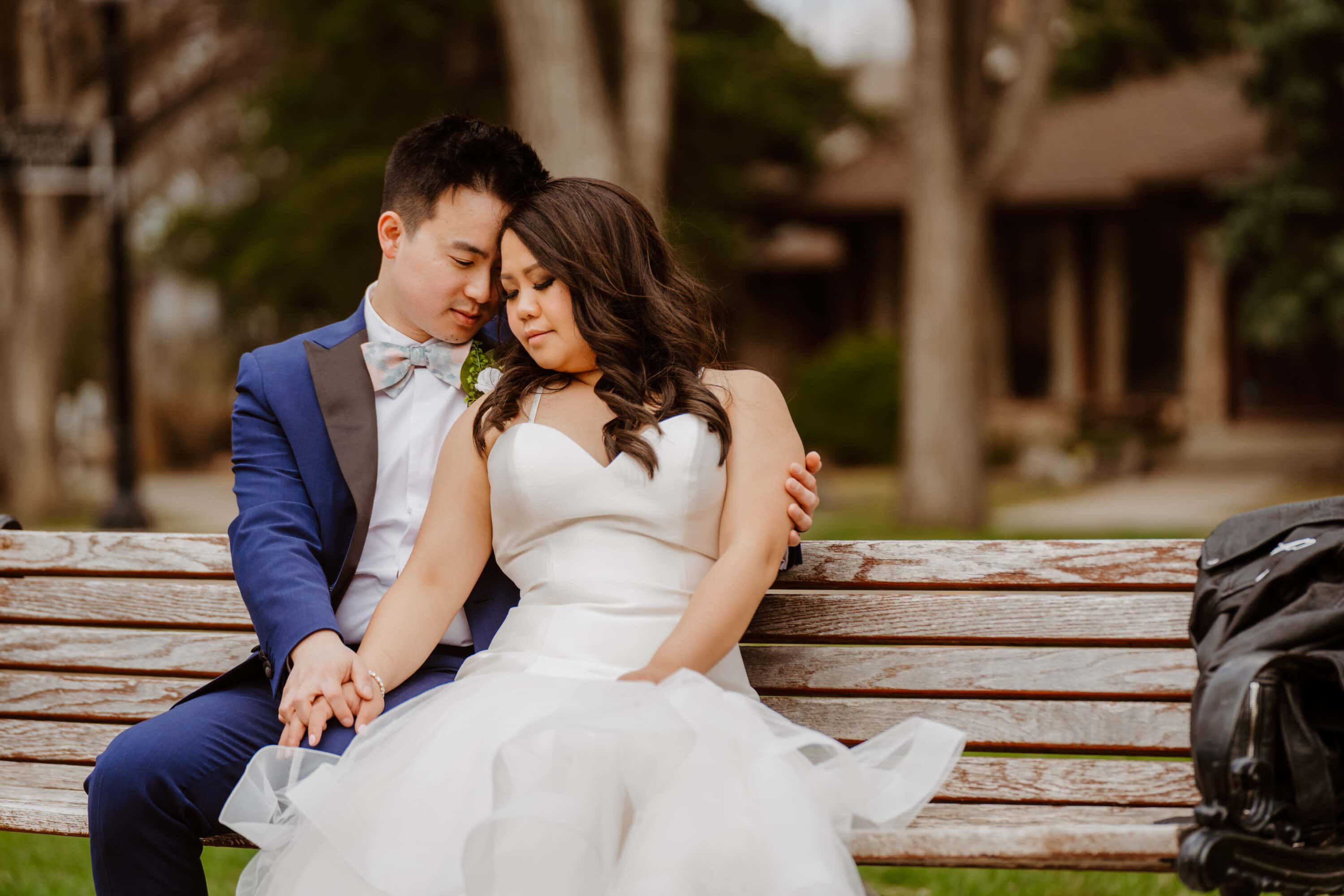 A bride and groom sitting on a bench outdoors and looking into each other's eyes