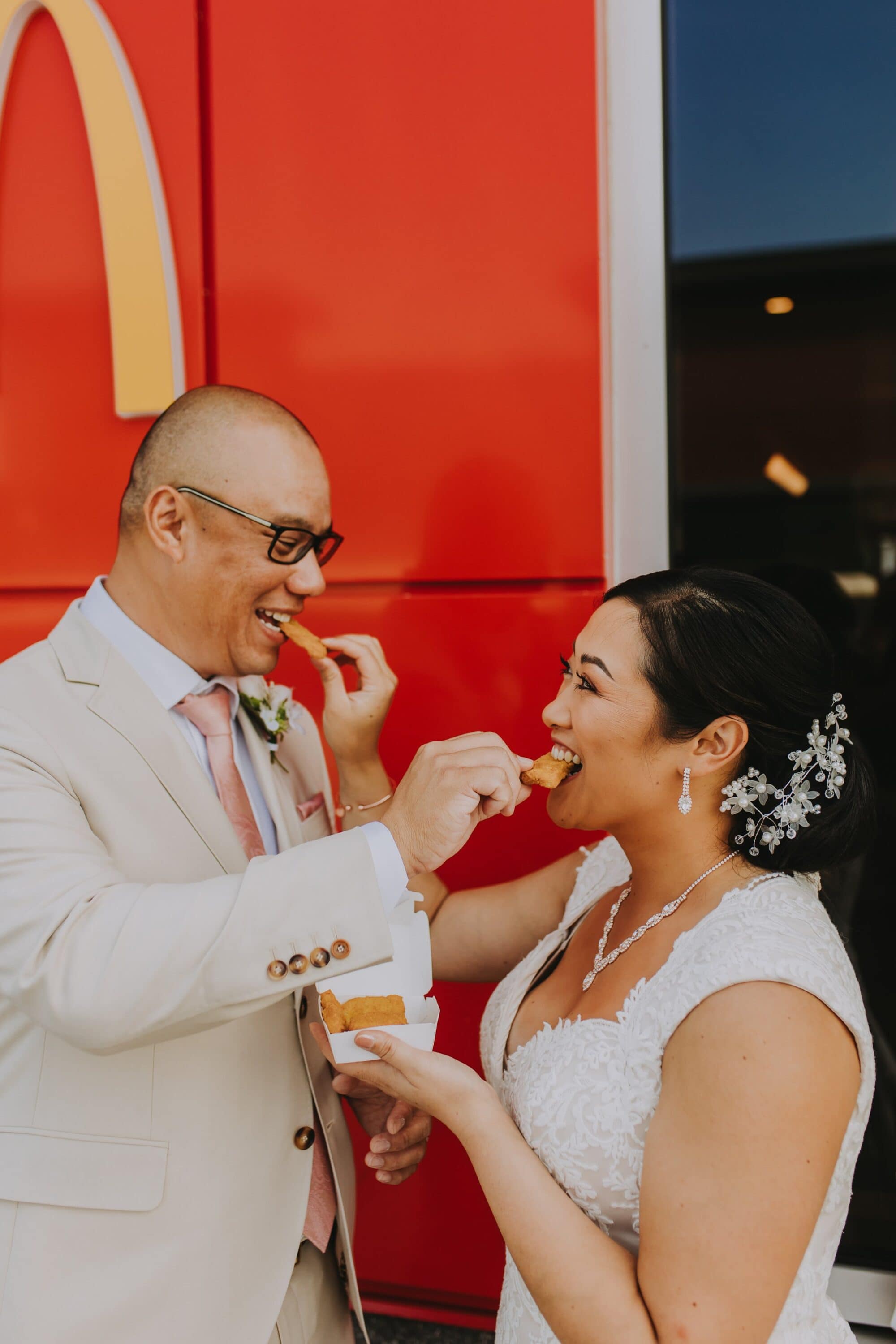 A bride and groom feeding each other chicken nuggets in front of Mcdonald's