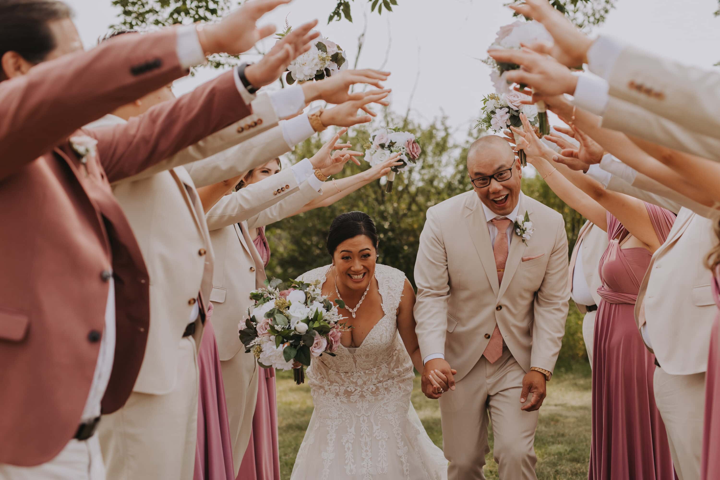 A wedding party is holding their arms up to create an arch, and the bride and groom are walking underneath