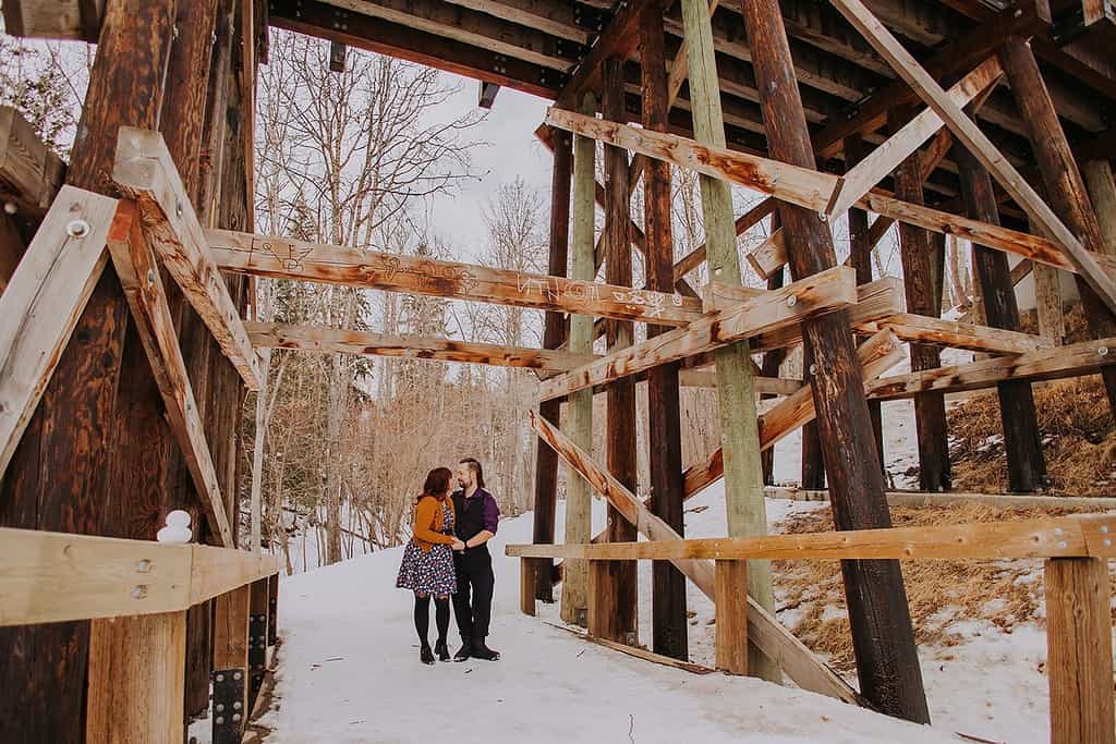 A couple standing underneath a wooden bridge during an engagement photography session in Mill Creek Ravine