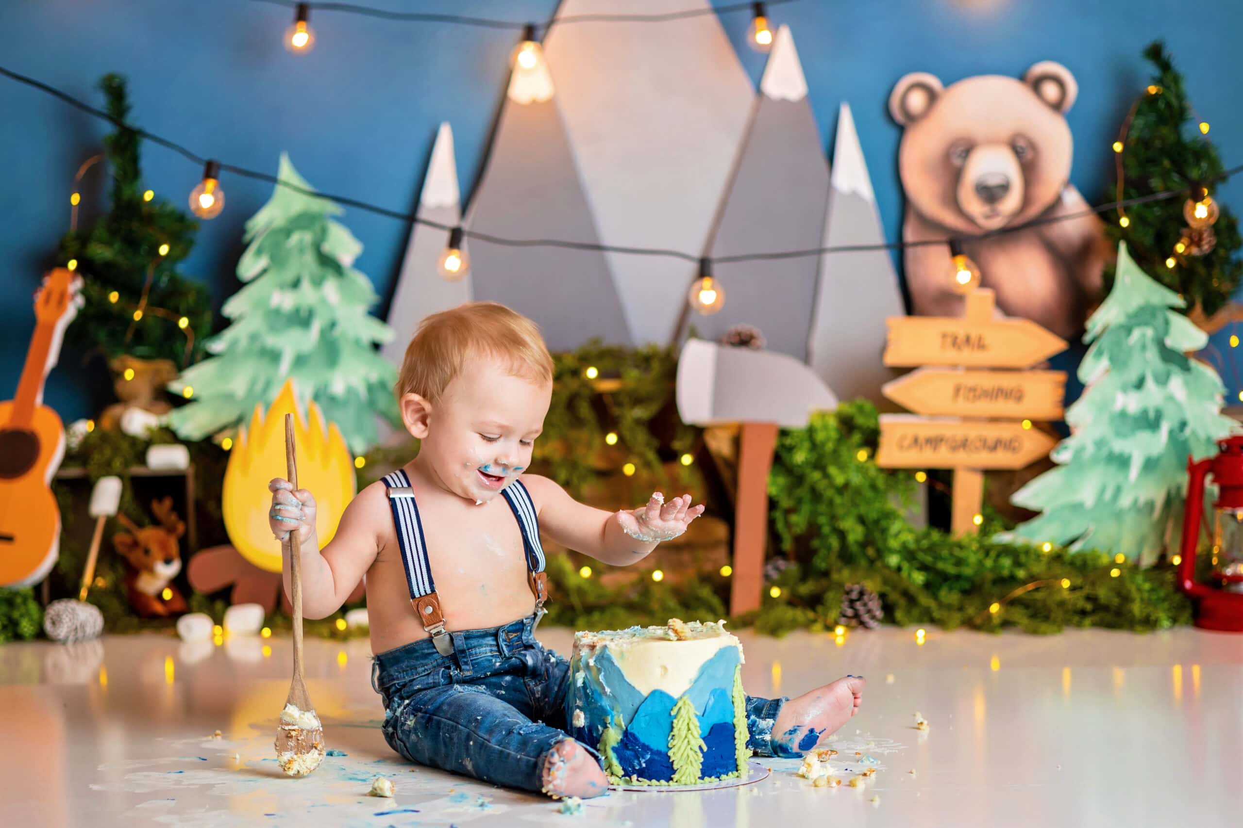 Camping Cake Smash Theme: A baby boy sits in front of a cake holding a wooden spoon