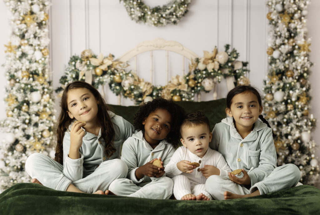 Siblings wearing PJs and sitting on a Christmas themed bed with cookies